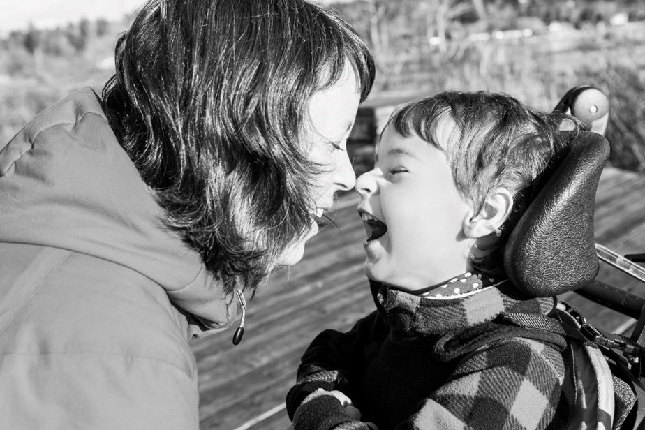In black and white. A woman touching her nose to her young child who is seated. They are both smiling.