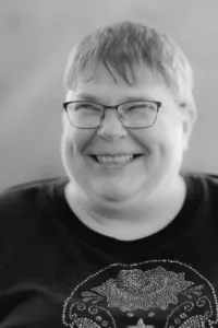 A black and white image of a woman with short light-coloured hair wearing glasses smiling and looking off to the side.