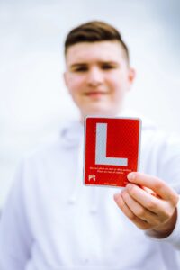 A teenage boy holds a small red learner's license sign up in front of him.