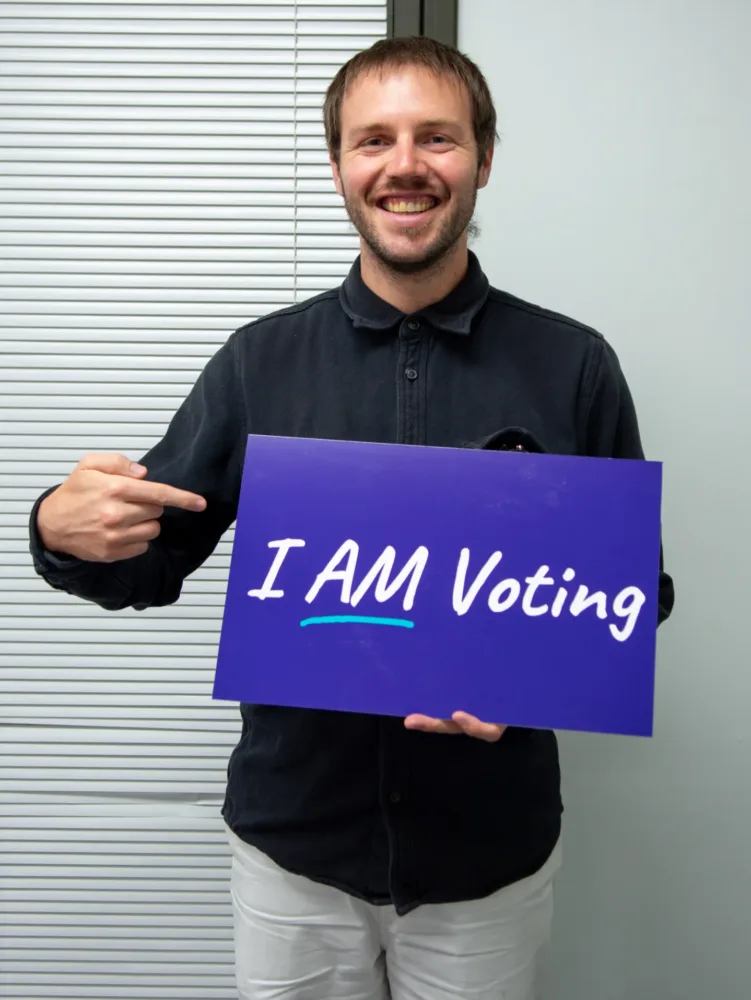 person holding and pointing to a sign that says "I am voting"